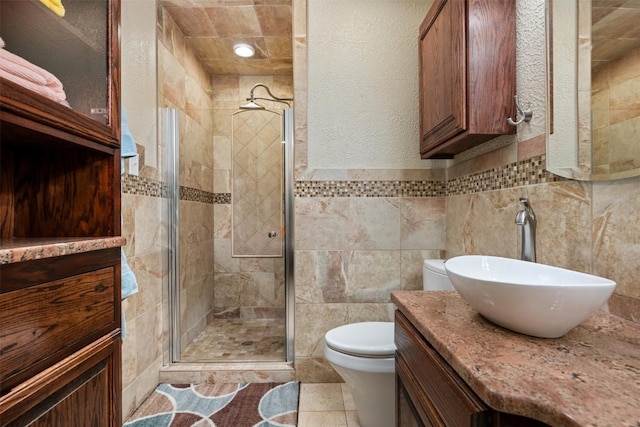 bathroom featuring vanity, a shower stall, tile walls, toilet, and a textured wall