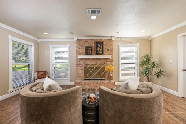 living room with wood finished floors, visible vents, baseboards, crown molding, and a brick fireplace