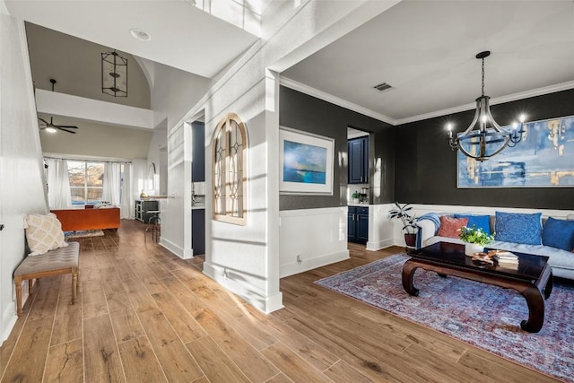 interior space with visible vents, crown molding, wainscoting, ceiling fan with notable chandelier, and wood finished floors