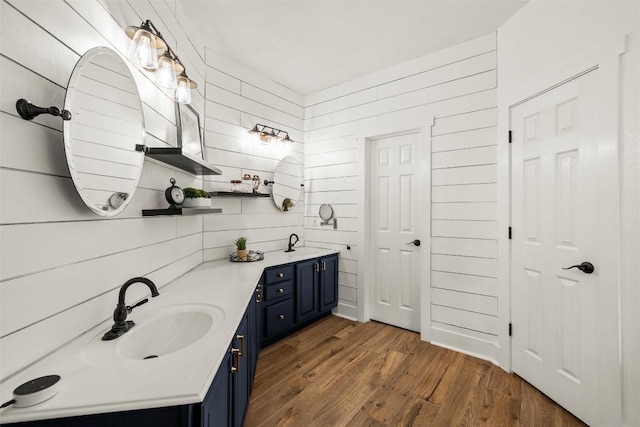 bathroom with a sink, wooden walls, wood finished floors, and double vanity