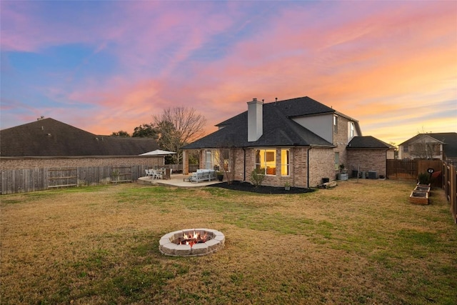 back of house featuring an outdoor fire pit, a chimney, a fenced backyard, a yard, and a patio area