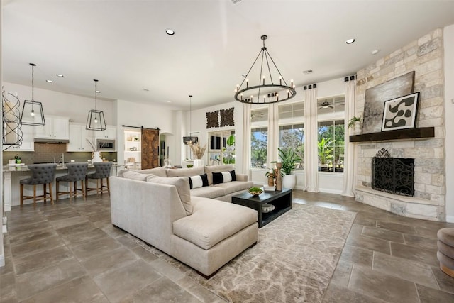 living room featuring recessed lighting, a stone fireplace, a barn door, a chandelier, and stone tile flooring