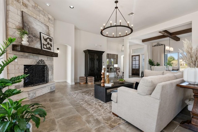 living area with visible vents, beam ceiling, a stone fireplace, an inviting chandelier, and baseboards