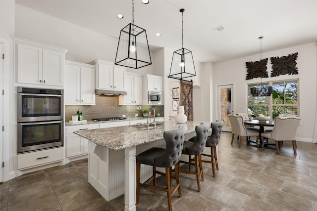 kitchen with appliances with stainless steel finishes, a sink, under cabinet range hood, tasteful backsplash, and white cabinetry