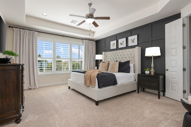 bedroom featuring a tray ceiling, light carpet, a ceiling fan, and baseboards