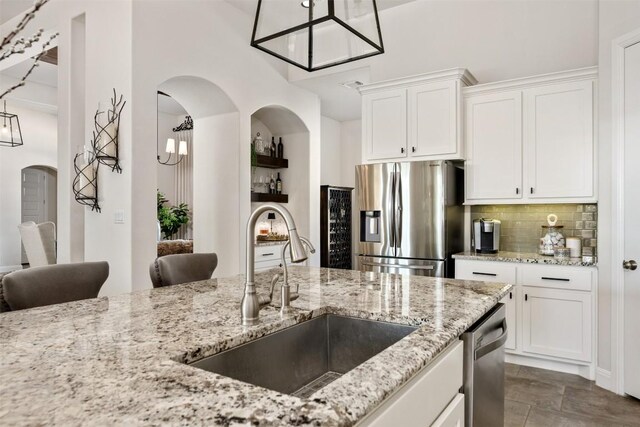 kitchen featuring stainless steel appliances, a sink, tasteful backsplash, arched walkways, and white cabinetry