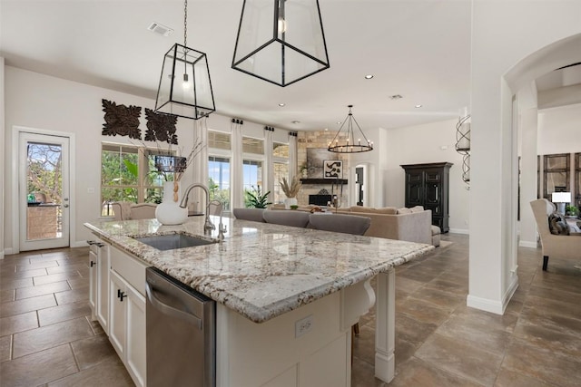 kitchen featuring a sink, dishwasher, arched walkways, white cabinets, and an island with sink