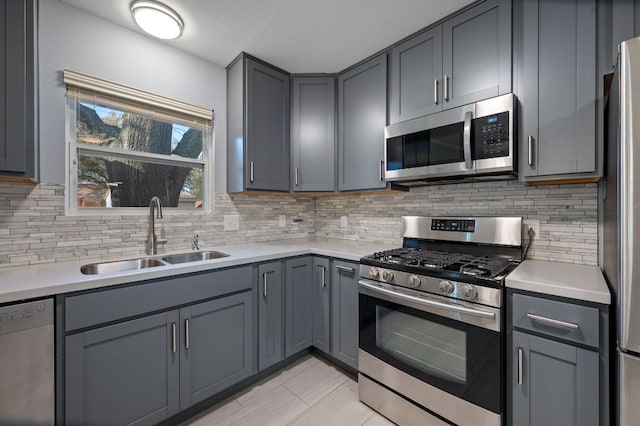 kitchen with backsplash, gray cabinets, appliances with stainless steel finishes, and a sink