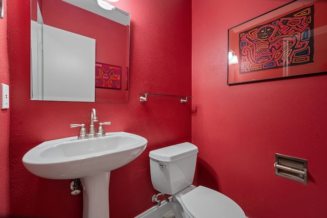 half bathroom featuring toilet and a textured wall