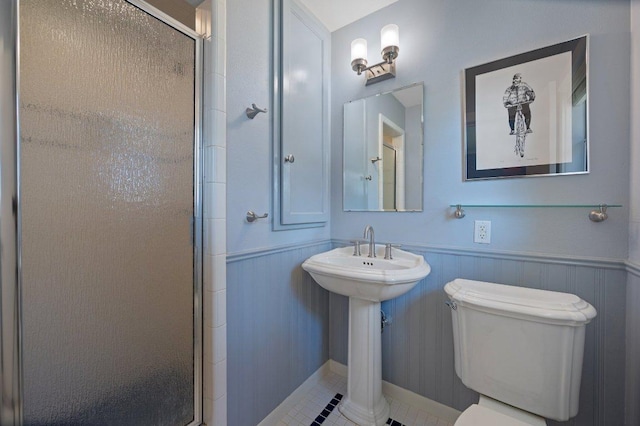 bathroom featuring a sink, toilet, a shower with door, and wainscoting