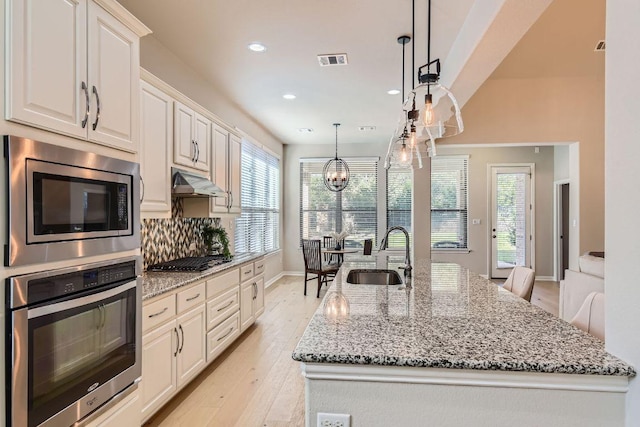 kitchen with visible vents, under cabinet range hood, light stone counters, appliances with stainless steel finishes, and a sink