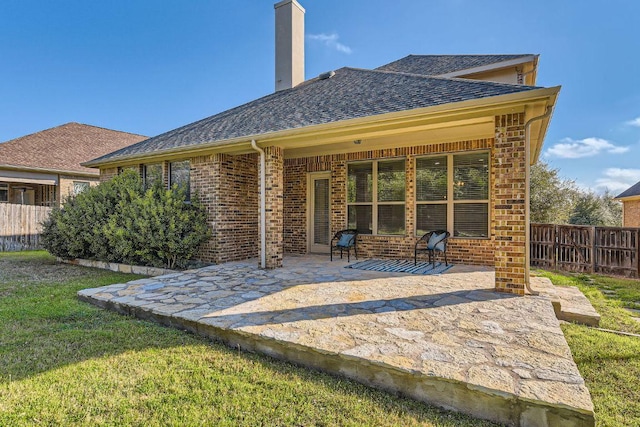 back of property with a patio, fence, a shingled roof, a chimney, and brick siding