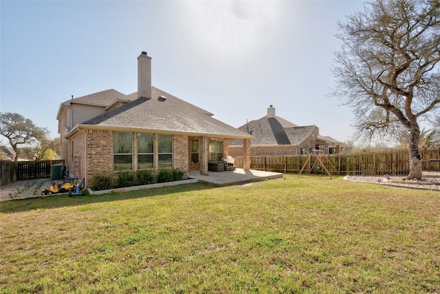 back of house featuring brick siding, a lawn, a chimney, a fenced backyard, and a patio