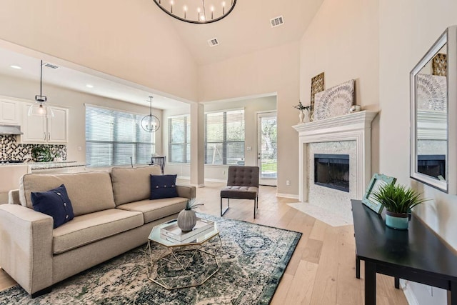 living room with a chandelier, light wood-style flooring, high vaulted ceiling, and a healthy amount of sunlight