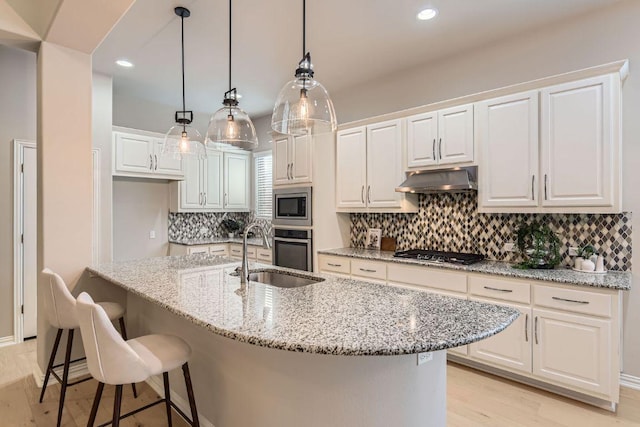 kitchen featuring a sink, white cabinets, under cabinet range hood, appliances with stainless steel finishes, and backsplash