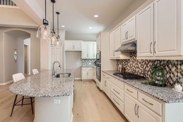 kitchen with under cabinet range hood, a breakfast bar area, light wood-type flooring, stainless steel appliances, and a sink