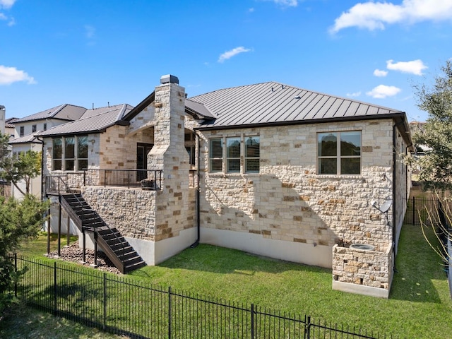 rear view of property with a lawn, a standing seam roof, stone siding, a fenced backyard, and metal roof