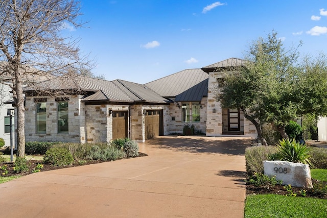 view of front facade with a standing seam roof, concrete driveway, a garage, stone siding, and metal roof