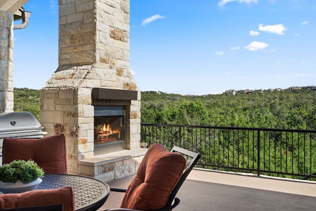 balcony featuring grilling area, an outdoor stone fireplace, and a wooded view