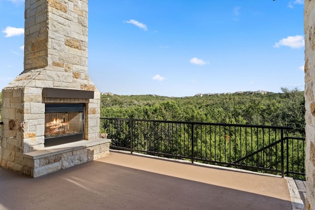 view of patio featuring a wooded view and an outdoor stone fireplace