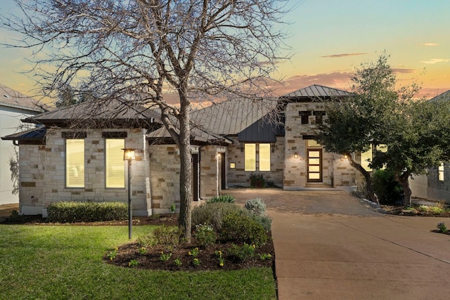 view of front of house featuring concrete driveway, a lawn, metal roof, stone siding, and a standing seam roof