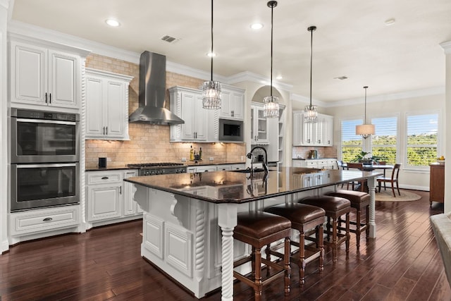 908 Crestone Stream Dr, Austin, TX 78738 - kitchen with wall chimney exhaust hood, appliances with stainless steel finishes, dark wood-style flooring, an island with sink, and a breakfast bar