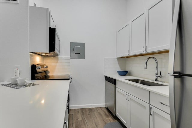 kitchen featuring wood finished floors, electric panel, a sink, light countertops, and appliances with stainless steel finishes