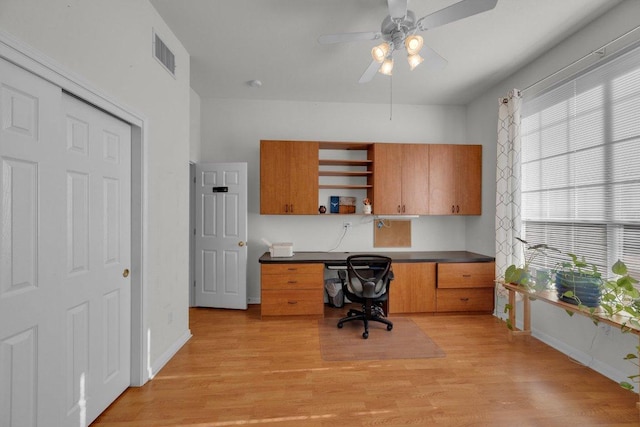 office space featuring light wood-style floors, visible vents, built in desk, and ceiling fan