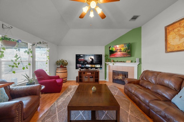 living area with visible vents, a tiled fireplace, wood finished floors, ceiling fan, and vaulted ceiling