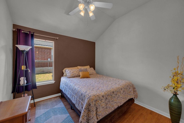 bedroom featuring baseboards, lofted ceiling, wood finished floors, and a ceiling fan