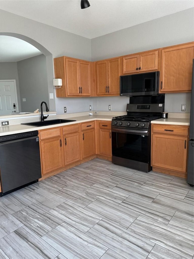 kitchen featuring arched walkways, black appliances, light countertops, and a sink