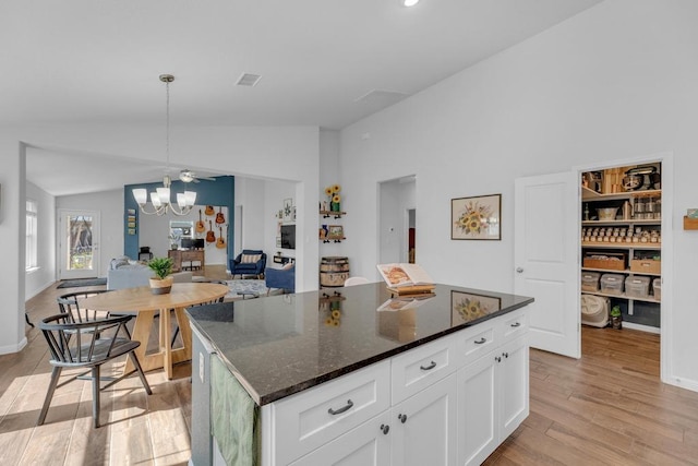 kitchen featuring an inviting chandelier, hanging light fixtures, vaulted ceiling, white cabinets, and light wood-type flooring