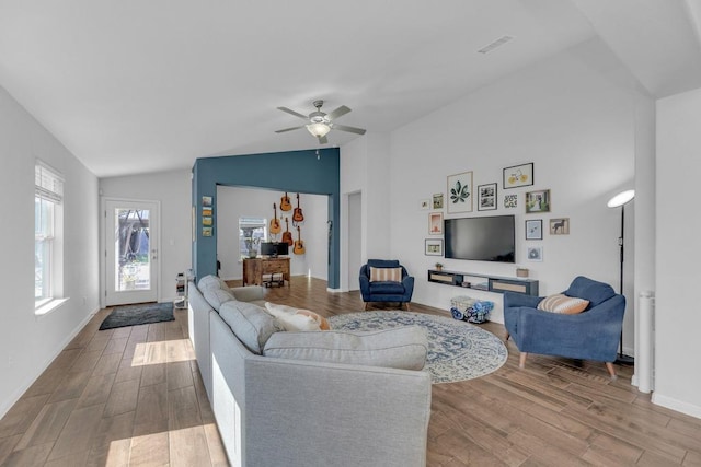 living area with a ceiling fan, wood finished floors, visible vents, baseboards, and vaulted ceiling