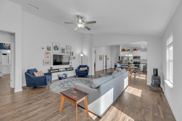 living room with visible vents, high vaulted ceiling, wood finished floors, ceiling fan, and a wood stove