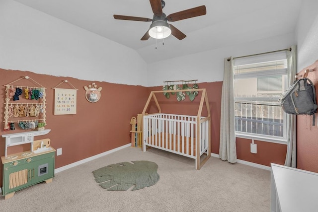 carpeted bedroom with a crib, a ceiling fan, baseboards, and vaulted ceiling