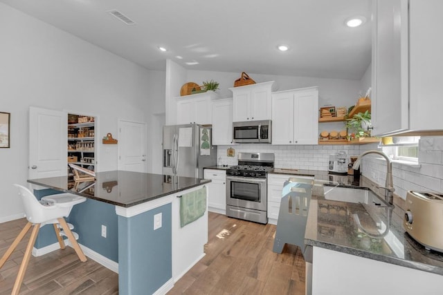 kitchen featuring visible vents, a sink, stainless steel appliances, light wood-style floors, and vaulted ceiling