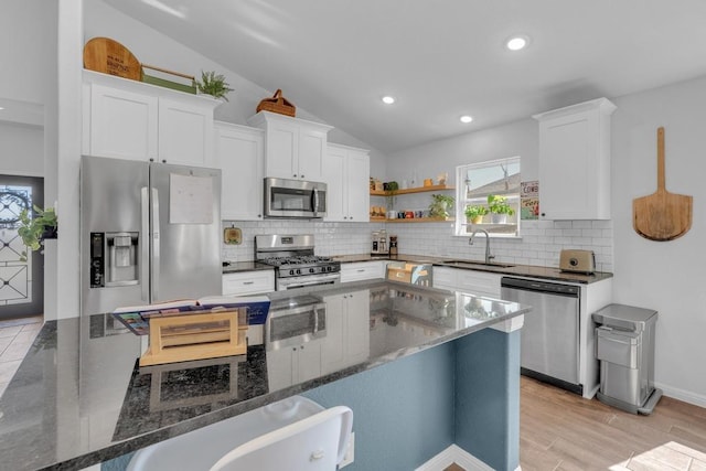 kitchen with a sink, white cabinetry, stainless steel appliances, dark stone counters, and lofted ceiling