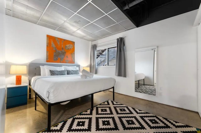 bedroom with a drop ceiling and concrete floors