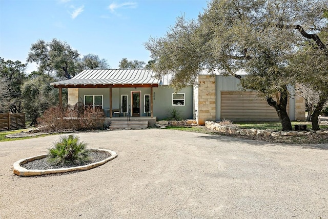 rear view of property with stone siding, curved driveway, a porch, and fence