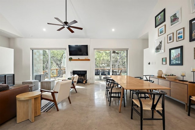 dining space with a ceiling fan, a healthy amount of sunlight, concrete flooring, and a fireplace with raised hearth