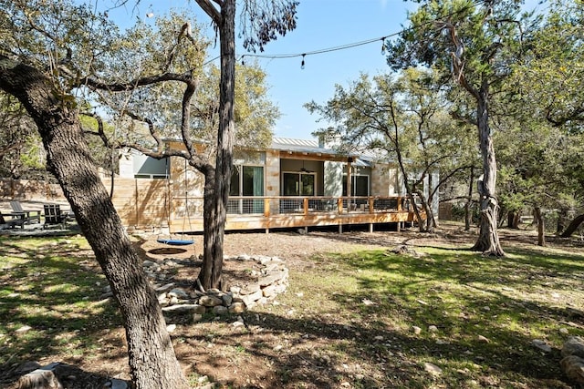 back of house with a wooden deck, a lawn, and metal roof