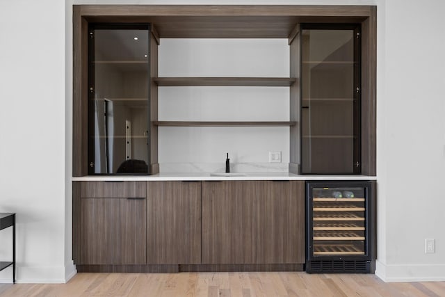 bar with baseboards, wine cooler, indoor wet bar, light wood-style flooring, and a sink