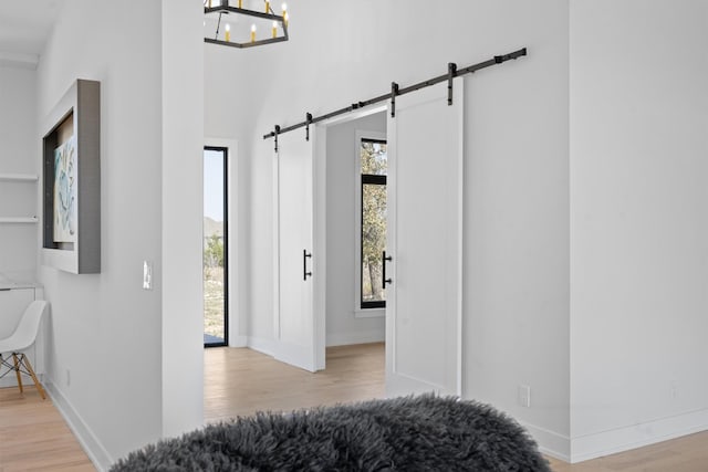 hallway featuring a barn door, plenty of natural light, wood finished floors, and baseboards