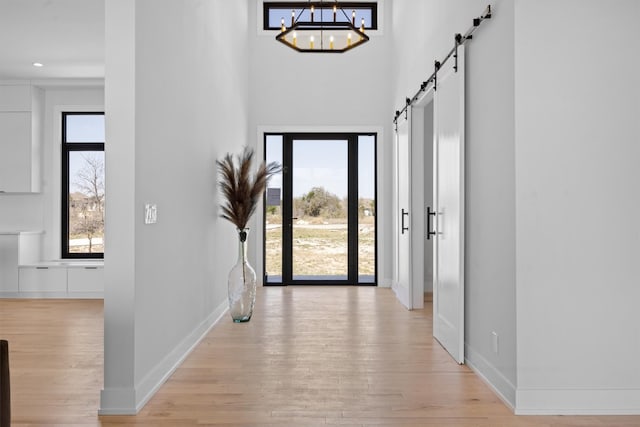 entrance foyer with baseboards, a chandelier, a barn door, light wood-style flooring, and a towering ceiling