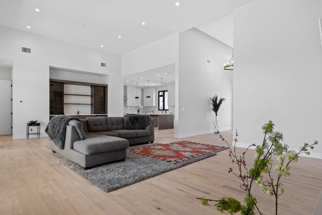 living area with an inviting chandelier, light wood-style flooring, visible vents, and a towering ceiling