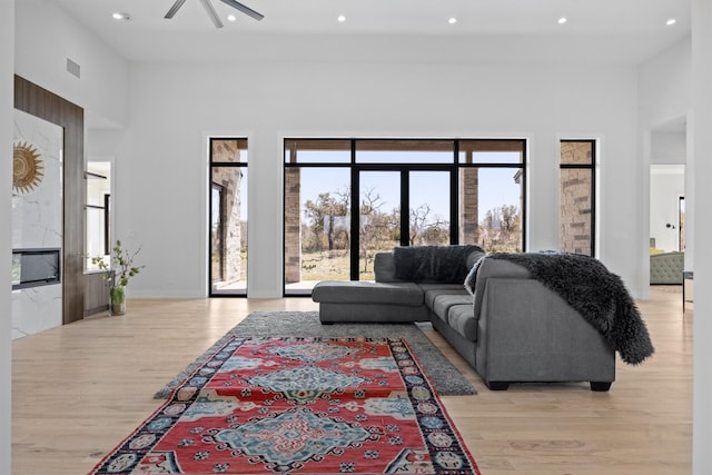 living area featuring visible vents, ceiling fan, recessed lighting, light wood-style floors, and a towering ceiling