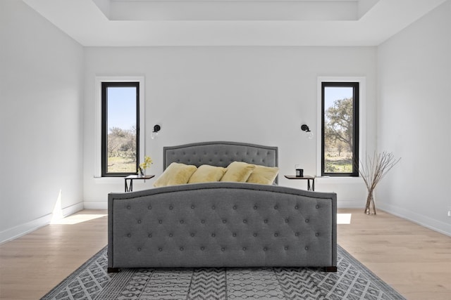 bedroom featuring light wood-type flooring, a raised ceiling, and baseboards