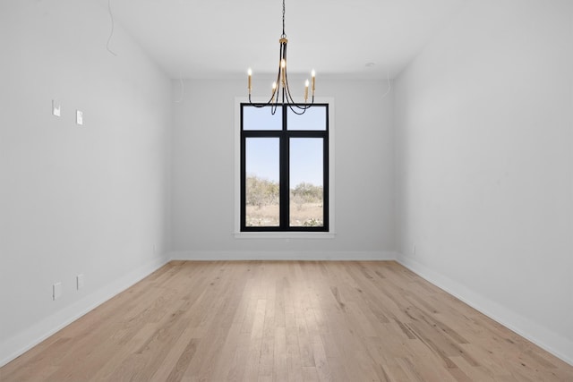 spare room with baseboards, a notable chandelier, and light wood-style flooring