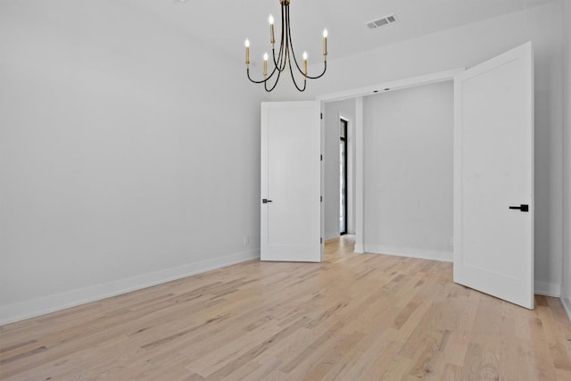 empty room featuring light wood finished floors, visible vents, baseboards, and an inviting chandelier