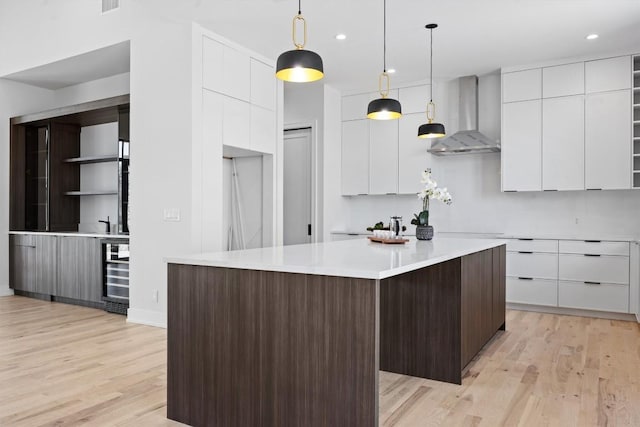 kitchen with white cabinets, modern cabinets, light wood-type flooring, and wall chimney range hood